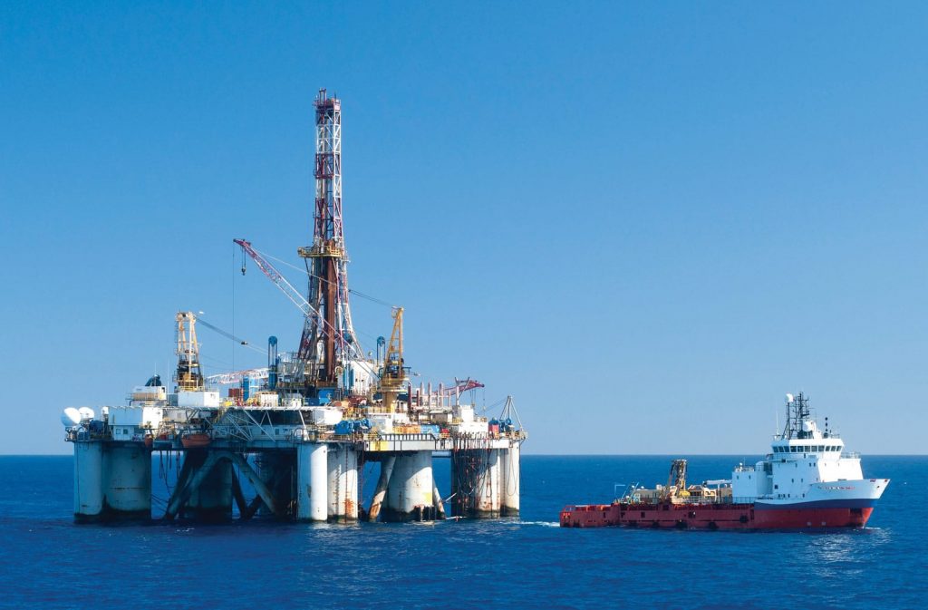 Offshore oil rig and supply vessel at sea under a clear sky.