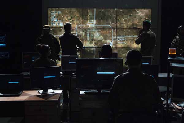 Eight employees of a defense agency in a control center with numerous desks and computer screens are looking at a large monitor using IHSE Government solutions. The global team of experts support clients working with mission critical data in signal processing, distribution, media conversion and many more.