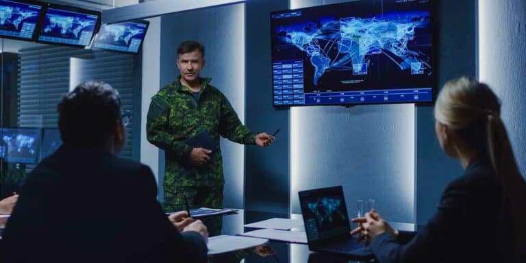 Military officer in camouflage uniform giving a security briefing in a high-tech conference room, pointing to 
a large screen displaying a digital world map with global network connections, while business professionals listen